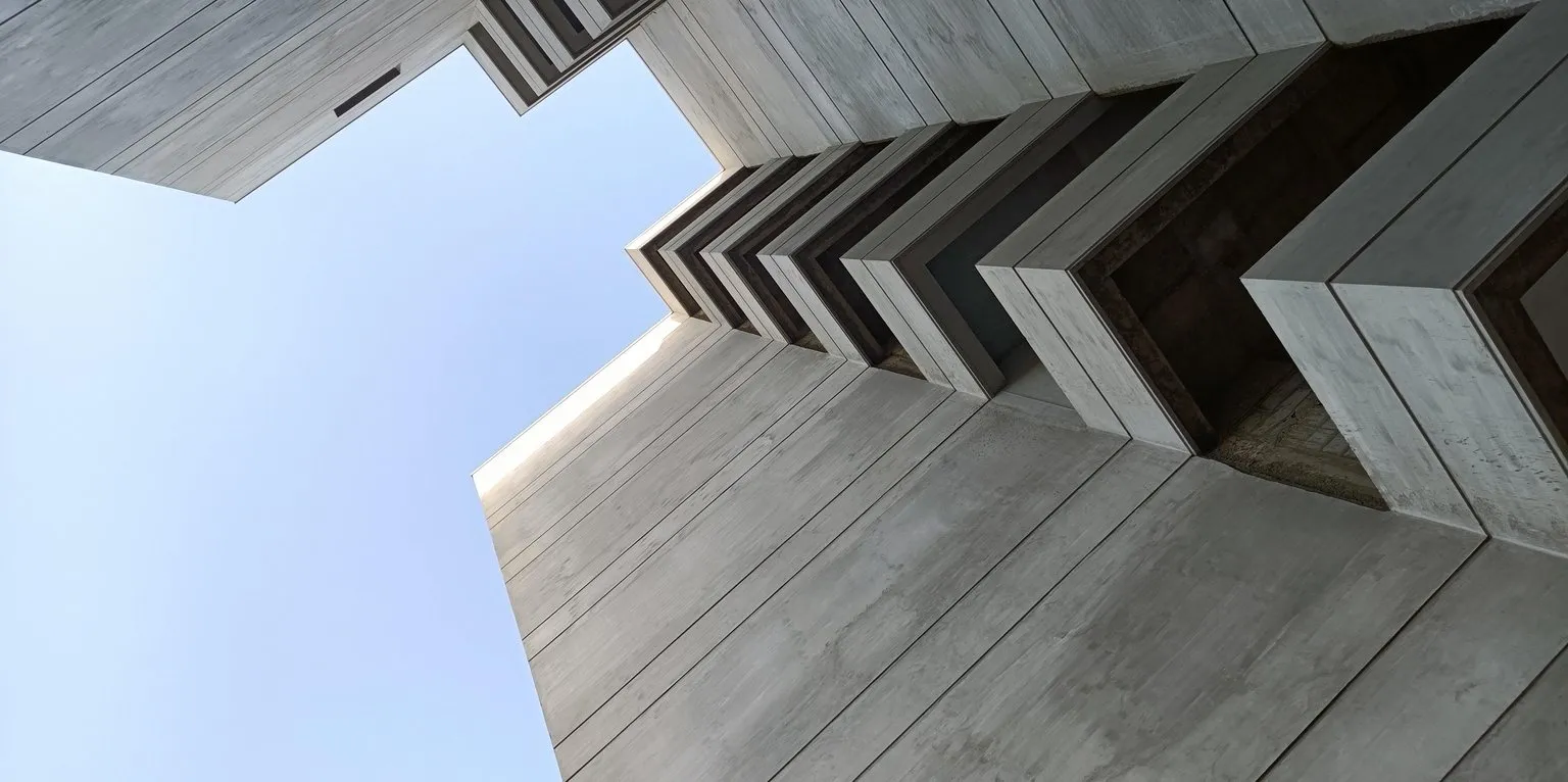 The corner of a concrete building seen looking straight up from its base, stepped soffits stacking away against open sky