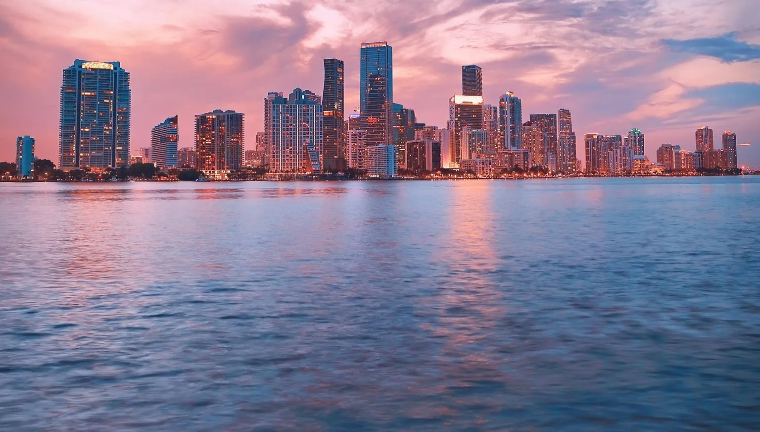 The Miami skyline at dusk under a pink and blue sky, seen across Biscayne Bay