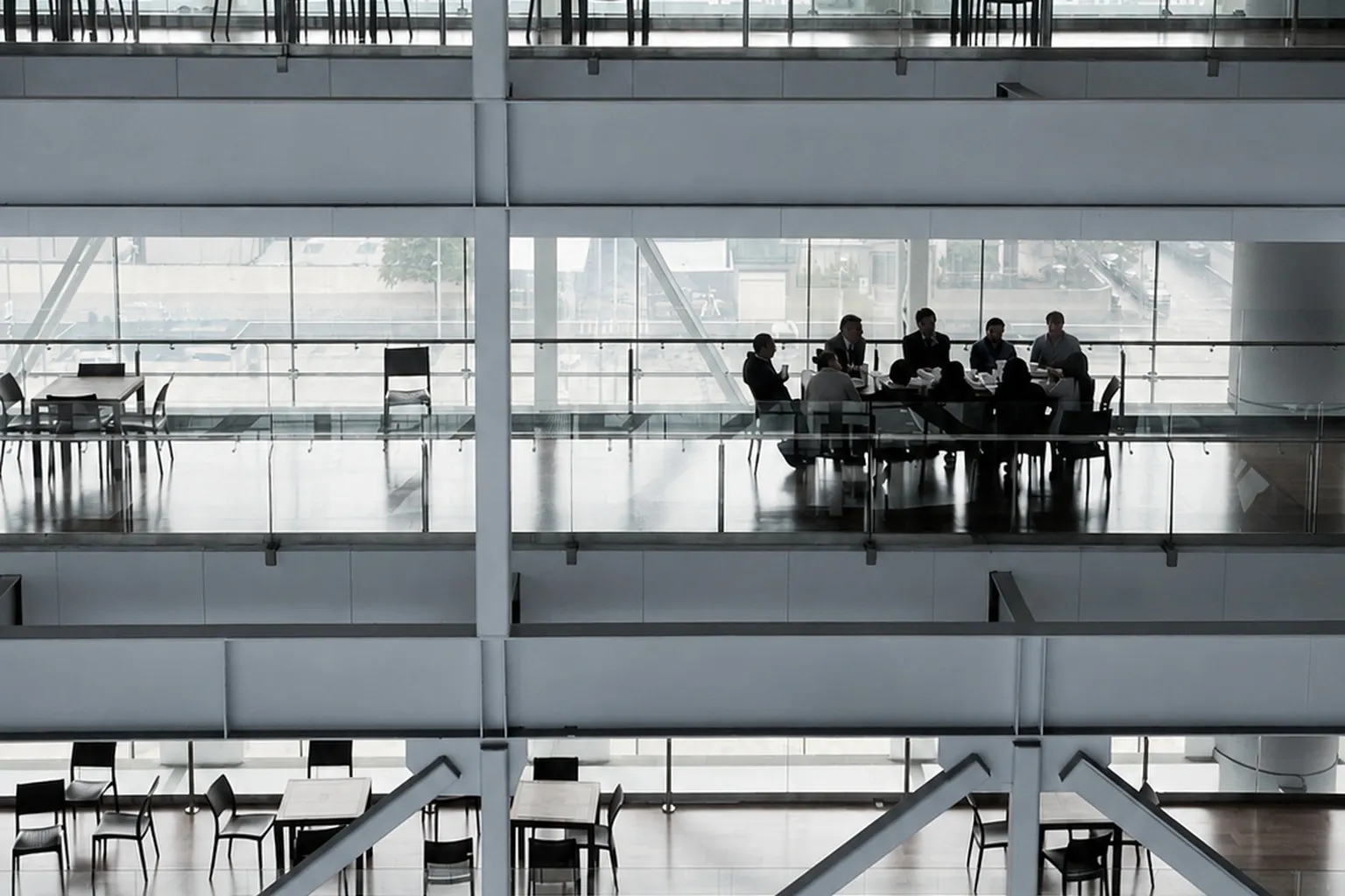 Colleagues in discussion around a table on one floor of a glass office building, seen across the atrium