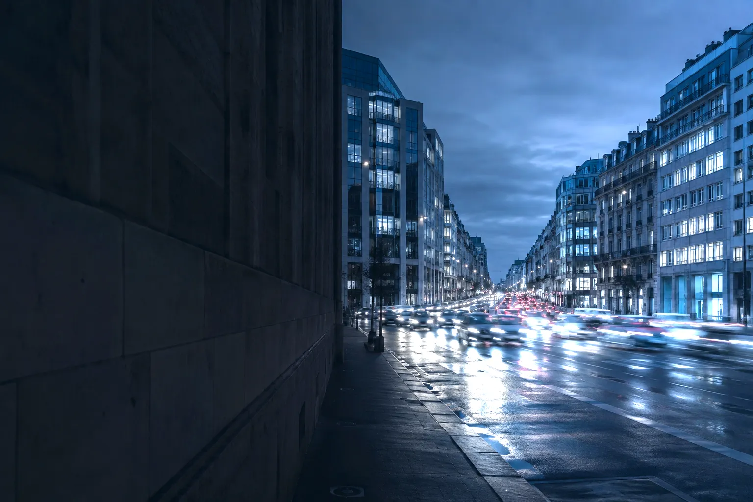 A city avenue at dusk, traffic moving between lit buildings