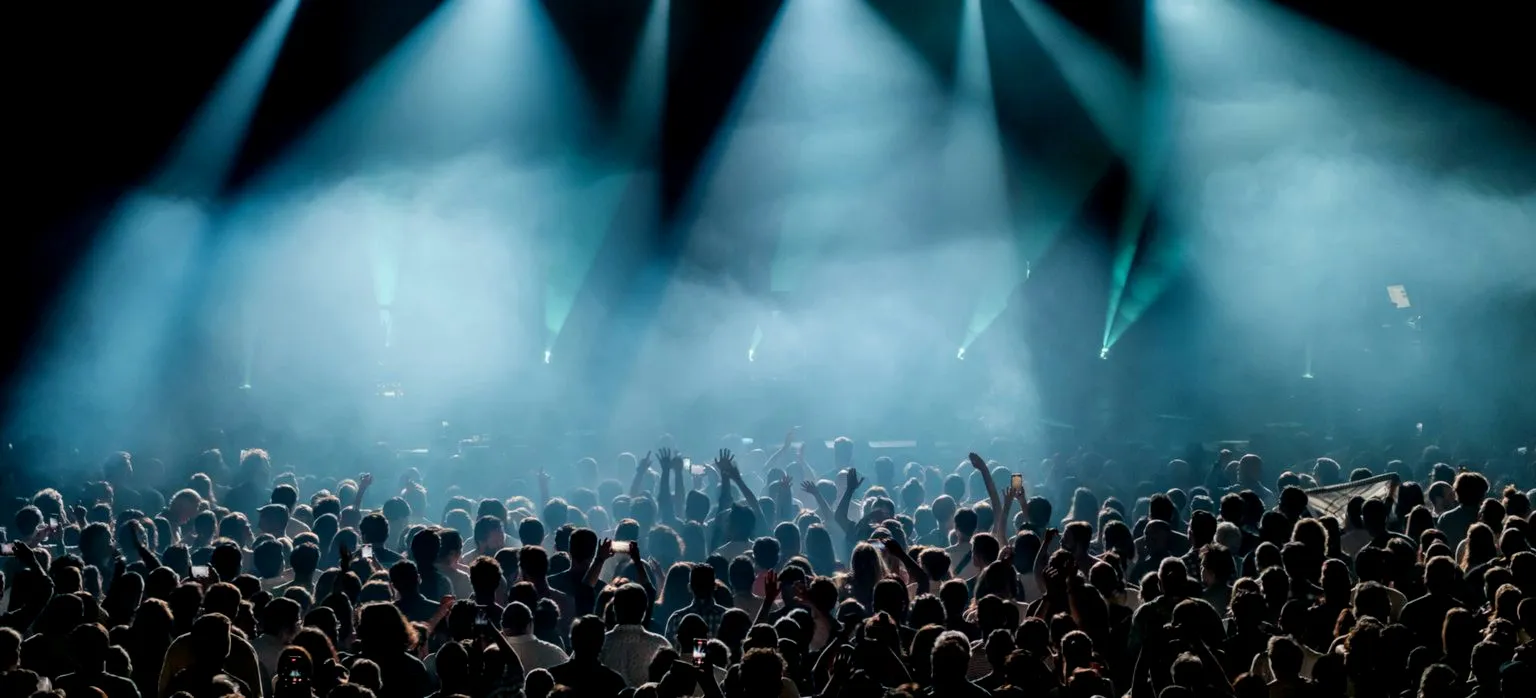 A crowd with raised hands beneath converging stage beams