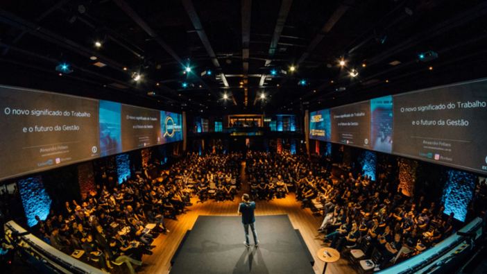 A speaker addressing a full auditorium from a lit stage